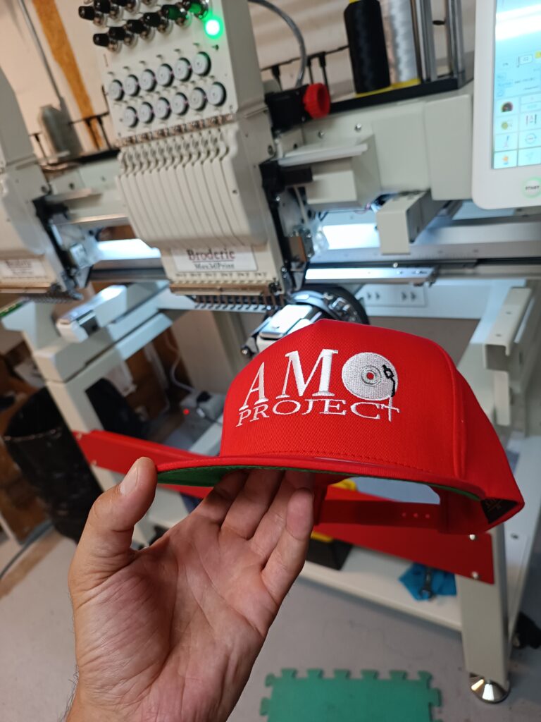 Casquette rouge brodée tenue devant une machine à broder industrielle